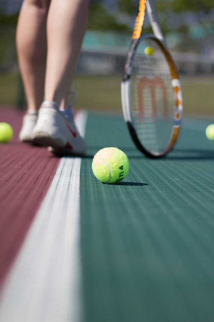 A tennis ball on a court with player legs in background.